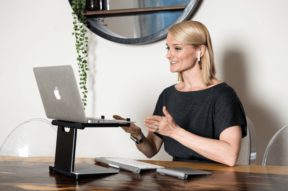 Professional woman presenting at standing desk with laptop, keyboard, and plant in modern workspace