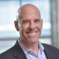 Professional headshot of smiling bald executive in dark suit and white shirt