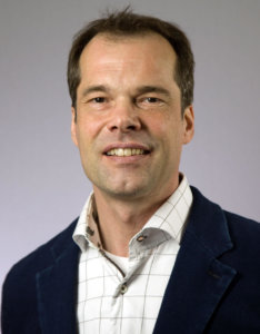 Professional headshot of William van Rossum smiling in navy blazer with white checkered shirt