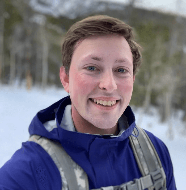 Portrait photo of person smiling outdoors in winter setting with blue jacket and snowy background