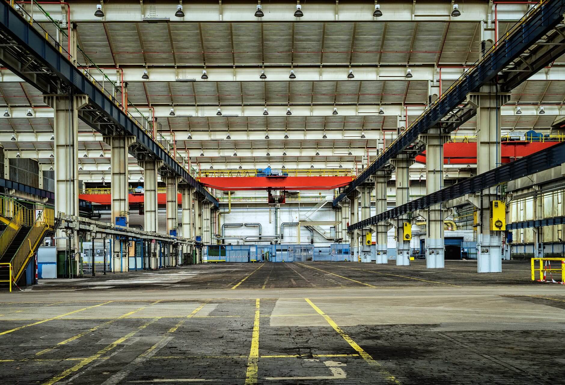 Large industrial warehouse interior with overhead cranes, equipment, and yellow floor markings